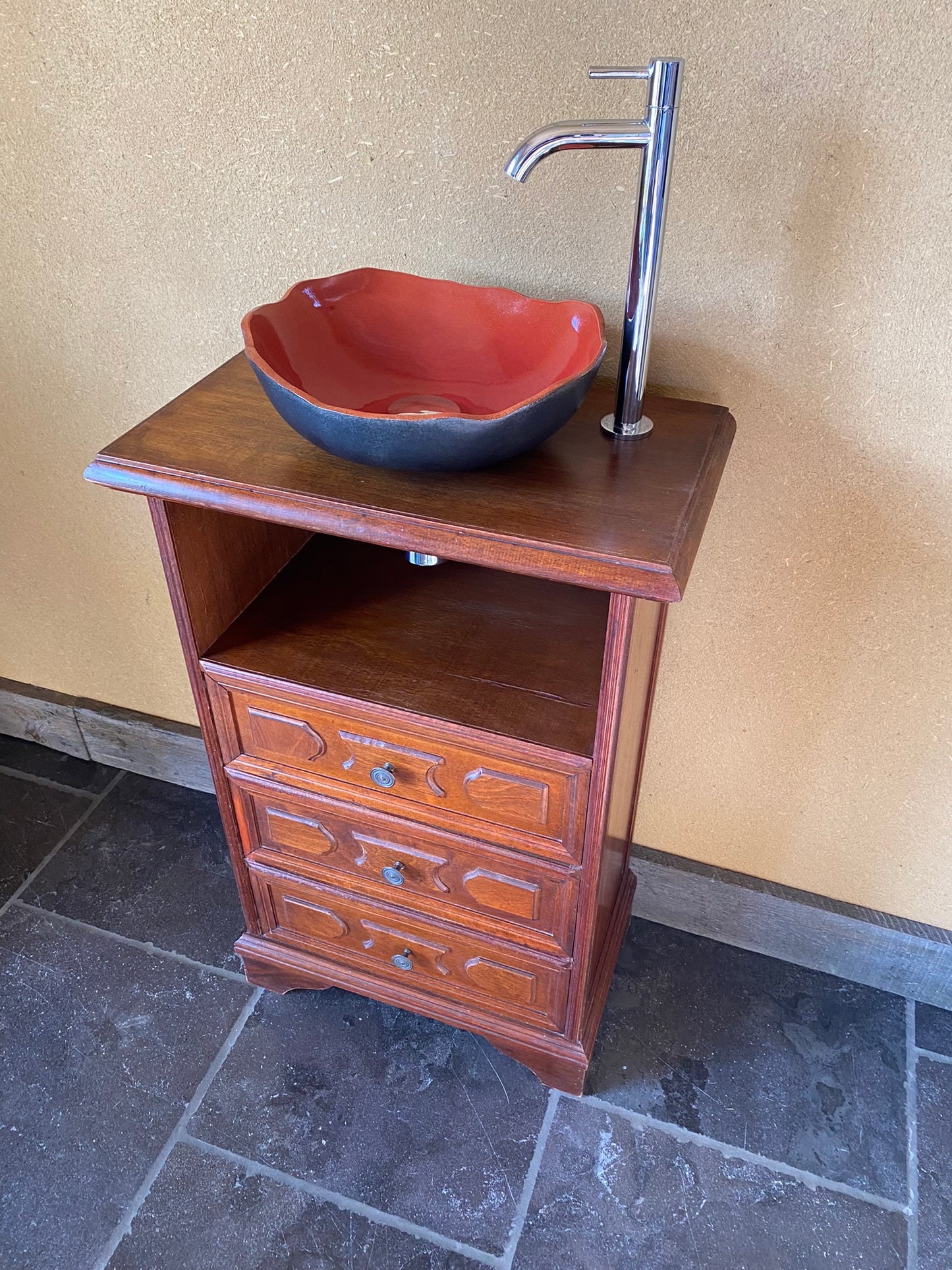 Vintage sanitair meubeltje met rode keramische spoelbak en een elegant kraantje